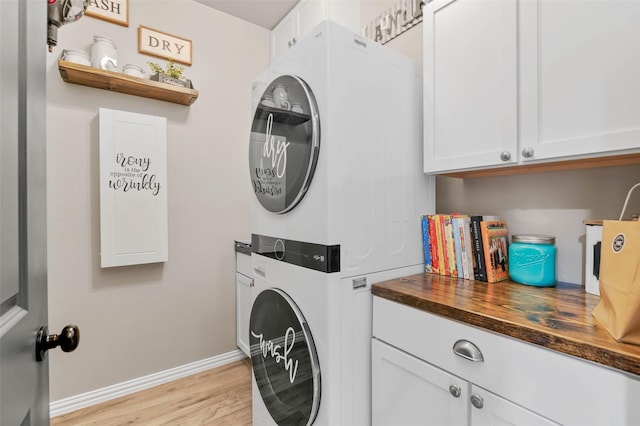 laundry area with light wood-type flooring, stacked washing maching and dryer, cabinet space, and baseboards