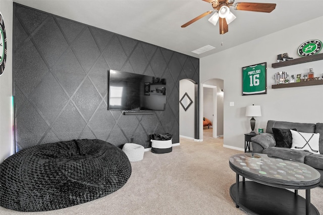 carpeted living area with arched walkways, an accent wall, ceiling fan, and baseboards