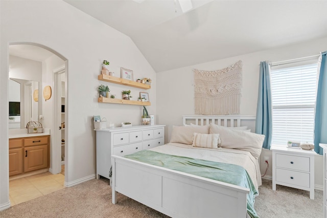 bedroom with arched walkways, light carpet, vaulted ceiling, ensuite bath, and baseboards