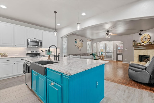 kitchen with stainless steel appliances, open floor plan, white cabinets, and light wood-style flooring