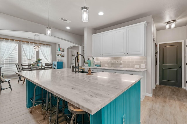 kitchen with arched walkways, a sink, visible vents, white cabinetry, and light wood-type flooring