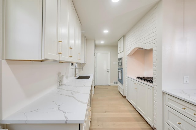 kitchen with recessed lighting, double oven, white cabinets, a sink, and light wood-type flooring