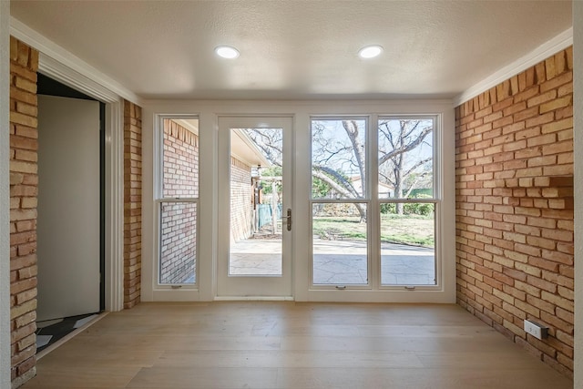 entryway featuring a textured ceiling, brick wall, and light wood-type flooring