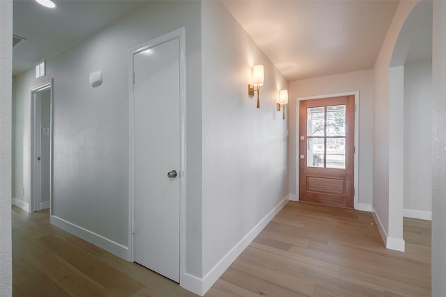 interior space with arched walkways, baseboards, visible vents, and light wood-style floors