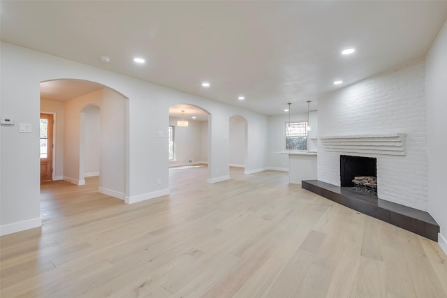 unfurnished living room with light wood-style floors, recessed lighting, a fireplace, and arched walkways