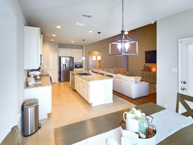 kitchen with arched walkways, stainless steel appliances, open floor plan, white cabinetry, and a sink