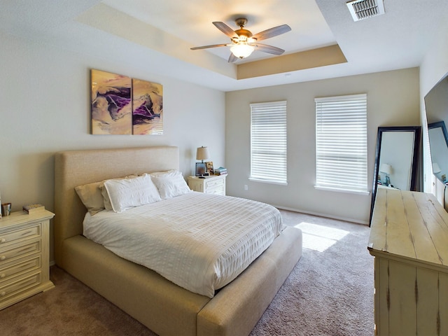 bedroom featuring visible vents, a tray ceiling, a ceiling fan, and light colored carpet