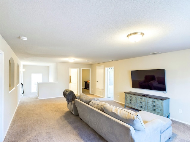 living room with a textured ceiling, baseboards, visible vents, and light colored carpet