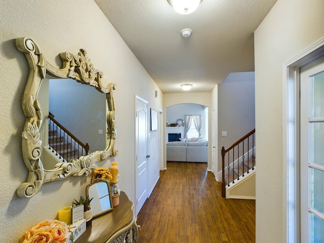 hall featuring baseboards, arched walkways, wood finished floors, stairs, and a textured ceiling