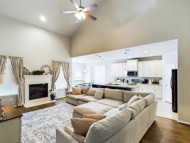 living room with dark wood-style floors, recessed lighting, a glass covered fireplace, ceiling fan, and high vaulted ceiling