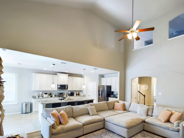 living area with visible vents, arched walkways, a ceiling fan, a towering ceiling, and stairs