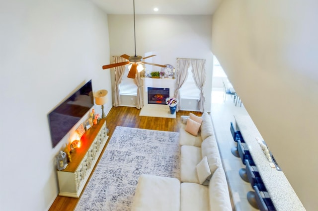 living room with wood finished floors, a glass covered fireplace, a towering ceiling, and a ceiling fan