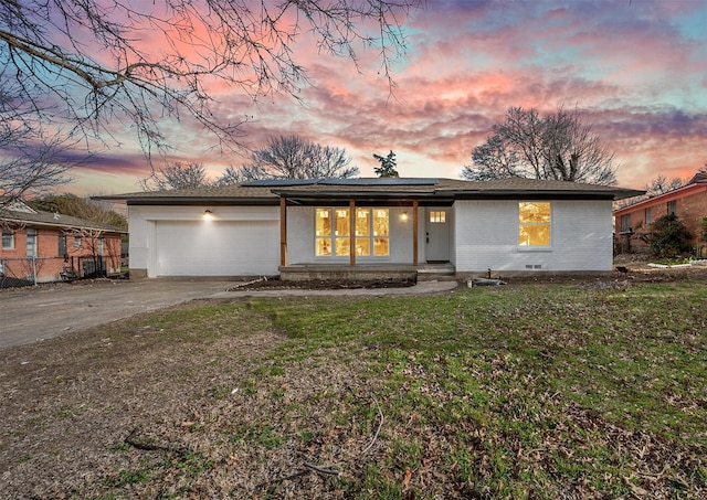 mid-century home featuring an attached garage, brick siding, concrete driveway, roof mounted solar panels, and a front yard