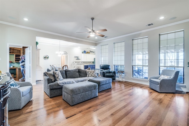 living room featuring light wood finished floors, visible vents, crown molding, and ceiling fan with notable chandelier