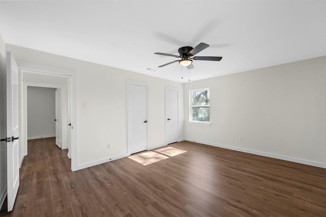 unfurnished bedroom featuring visible vents, baseboards, a ceiling fan, wood finished floors, and two closets