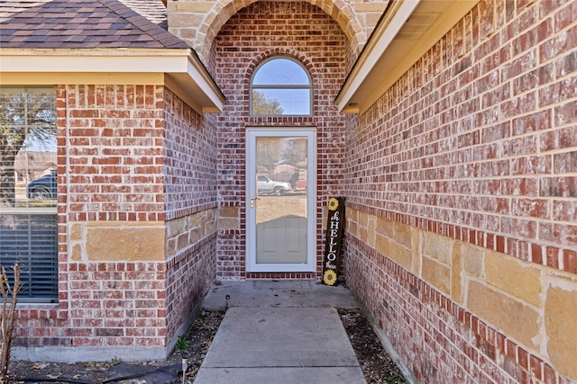 property entrance with a shingled roof and brick siding