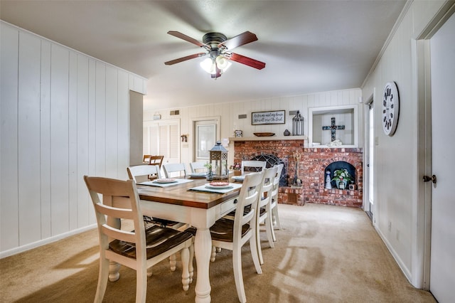 dining room with baseboards, light colored carpet, a brick fireplace, and a ceiling fan