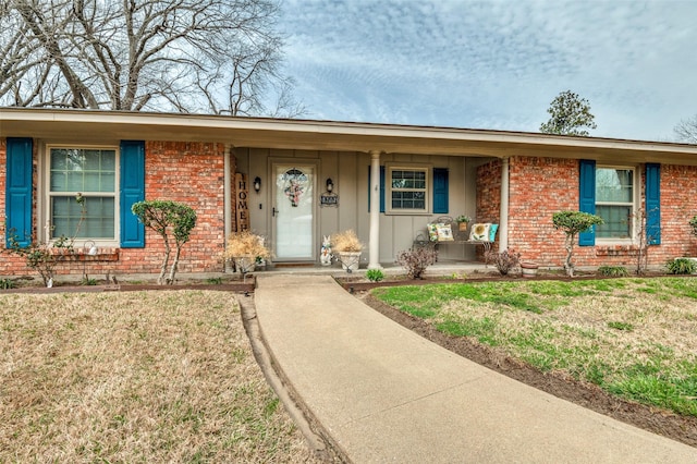 single story home featuring board and batten siding, a front yard, a porch, and brick siding