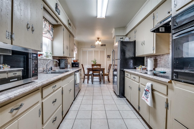 kitchen featuring under cabinet range hood, light countertops, light tile patterned floors, black appliances, and a sink