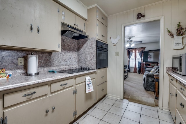 kitchen with under cabinet range hood, light countertops, ornamental molding, light tile patterned floors, and black appliances