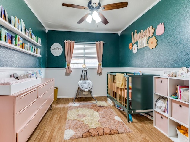 bedroom with a ceiling fan, ornamental molding, wood finished floors, and wainscoting