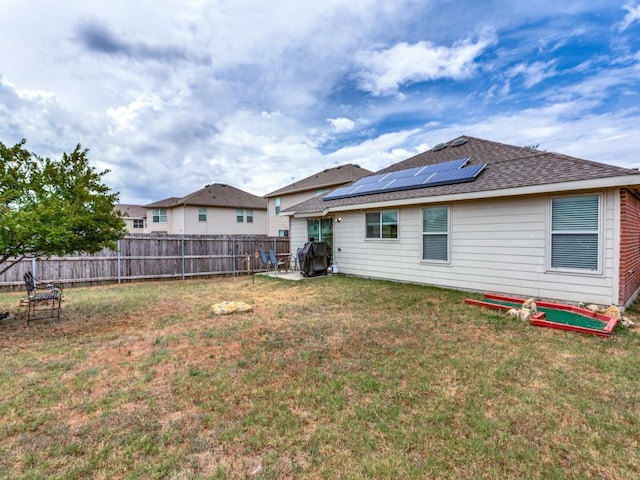 rear view of property featuring roof mounted solar panels, a fenced backyard, a lawn, and roof with shingles