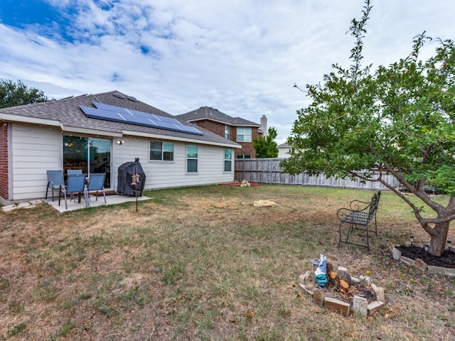 rear view of property with a patio, fence, a yard, roof with shingles, and roof mounted solar panels