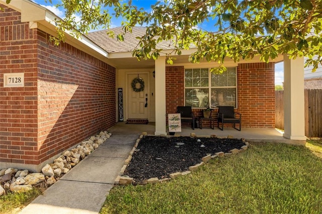 entrance to property featuring a porch, brick siding, fence, and roof with shingles