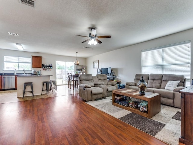 living area featuring a textured ceiling, light wood finished floors, visible vents, and a ceiling fan