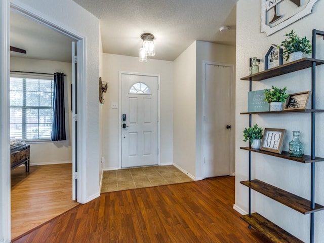 foyer featuring a textured ceiling, baseboards, and wood finished floors