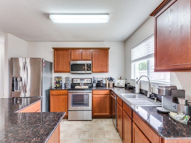 kitchen featuring brown cabinetry, a sink, dark stone countertops, and appliances with stainless steel finishes
