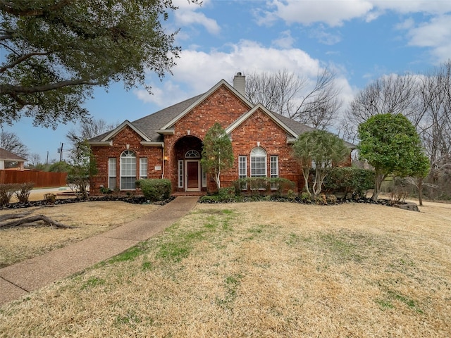 traditional-style home featuring a front yard, a shingled roof, a chimney, and brick siding