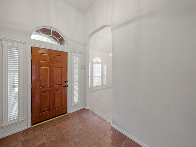 foyer featuring arched walkways, dark carpet, a high ceiling, dark tile patterned flooring, and baseboards