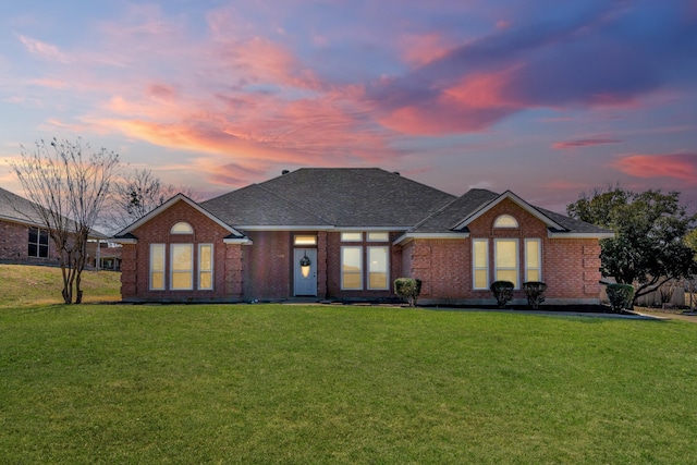 back of house with brick siding, roof with shingles, and a yard