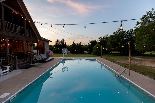 pool at dusk featuring a patio, a lawn, and an outdoor pool