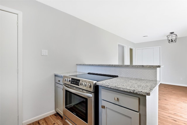 kitchen with light wood-style flooring, backsplash, electric range, gray cabinetry, and baseboards