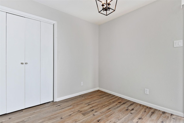 unfurnished bedroom featuring a closet, an inviting chandelier, wood finished floors, and baseboards