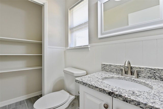 half bathroom with a wainscoted wall, vanity, and toilet