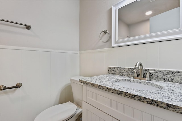 half bathroom featuring a wainscoted wall, vanity, and toilet