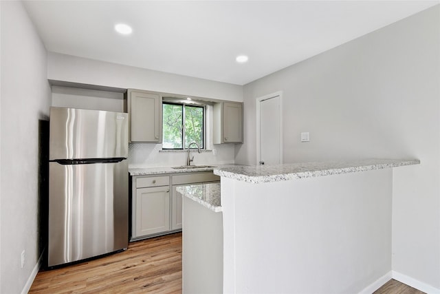 kitchen with freestanding refrigerator, light stone countertops, gray cabinetry, light wood-style floors, and a sink