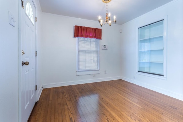 unfurnished room featuring ornamental molding, baseboards, an inviting chandelier, and hardwood / wood-style flooring