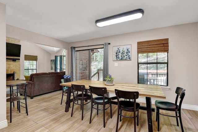 dining room featuring light wood-style floors, vaulted ceiling, a stone fireplace, and baseboards