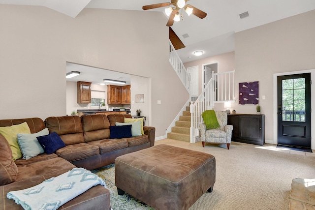 living room with visible vents, light carpet, high vaulted ceiling, baseboards, and stairs