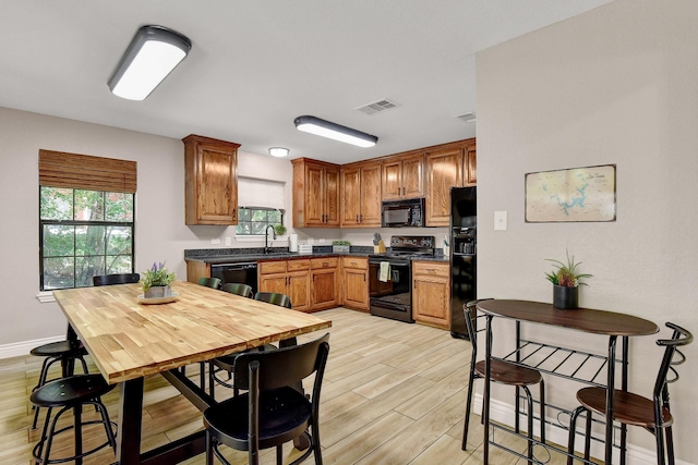 kitchen featuring dark countertops, visible vents, a sink, light wood-type flooring, and black appliances