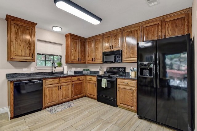 kitchen with brown cabinets, light wood finished floors, visible vents, a sink, and black appliances