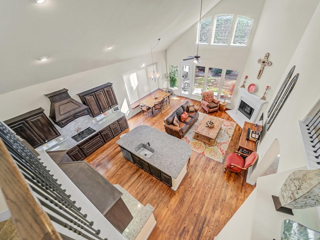 living room with high vaulted ceiling, ceiling fan with notable chandelier, wood finished floors, a fireplace with flush hearth, and stairs