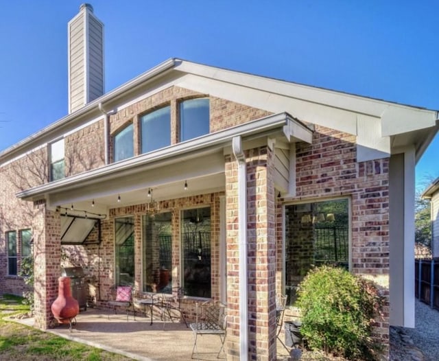 rear view of house featuring a chimney, a patio, and brick siding