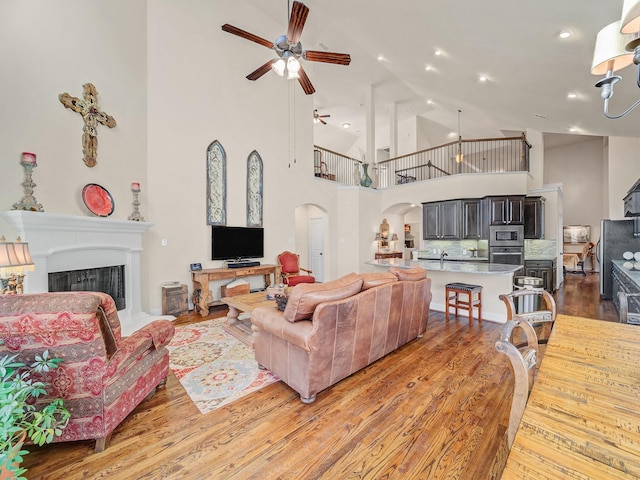 living area with arched walkways, a fireplace, light wood-style flooring, a ceiling fan, and high vaulted ceiling