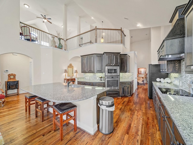 kitchen featuring arched walkways, appliances with stainless steel finishes, light stone countertops, a kitchen bar, and custom range hood