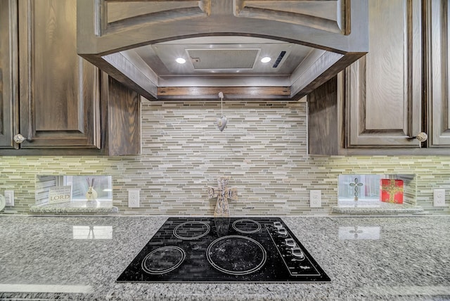 kitchen with custom exhaust hood, backsplash, black electric cooktop, and light stone countertops